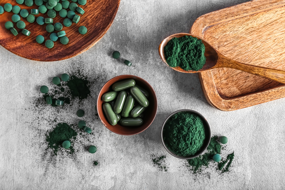 Bowls of spirulina powder and pills on grunge background
