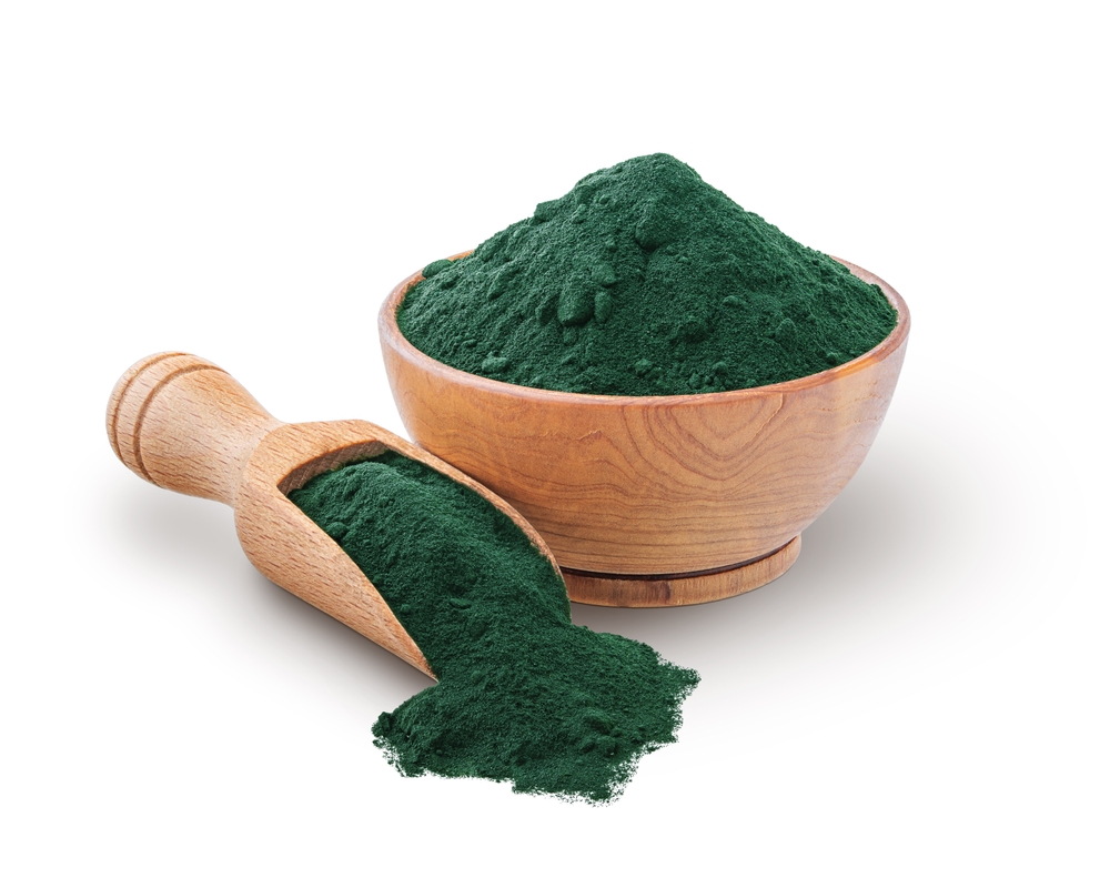 Wooden scoop and bowl full of spirulina powder isolated on white

