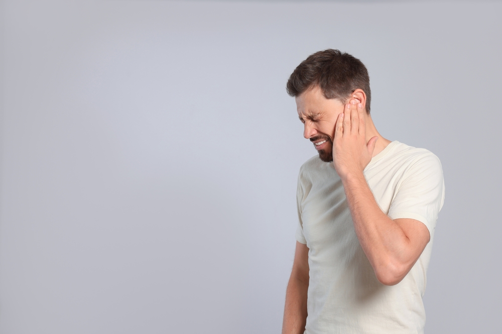 Man suffering from ear pain on grey background
