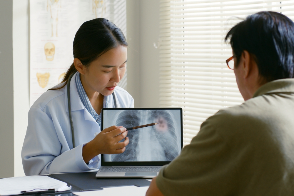 Young Asian woman doctor showing lung x-ray test results and describe to a senior patient in hospital. For cancer awareness month

