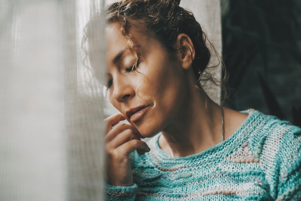 Exhausted and sad woman alone at home near the window with closed eyes and depressed expression on face. Closeup portrait of adult female people with sadness. People and mental burnout problems life
