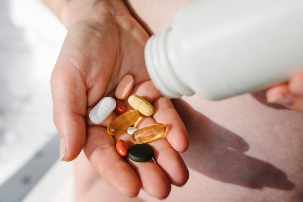 Closeup photo of supplements with a white bottle. Pregnant woman take omega 3, multivitamins, vitamins B, C, D, collagen tablets, probiotics, iron capsule. Girl hold vitamins daily. Top view.
