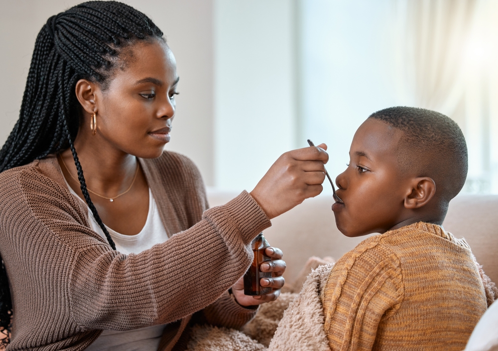 This will make you feel better. a young mother giving her sick son cough syrup at home.
