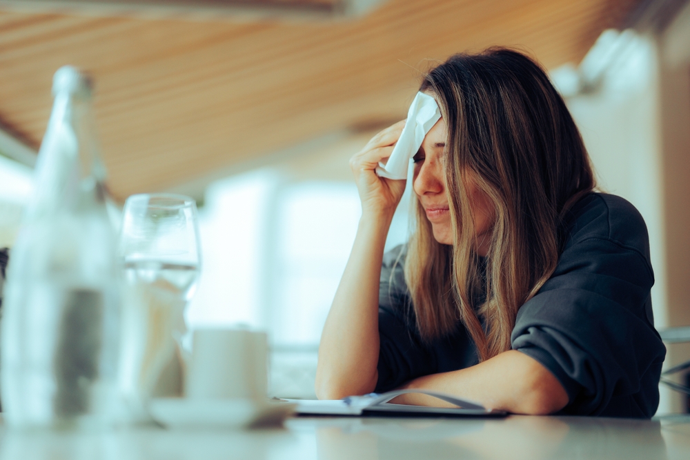 Woman Wiping Sweaty Forehead Using a Napkin. Lady suffering from hot flashes due to early menopause symptoms
