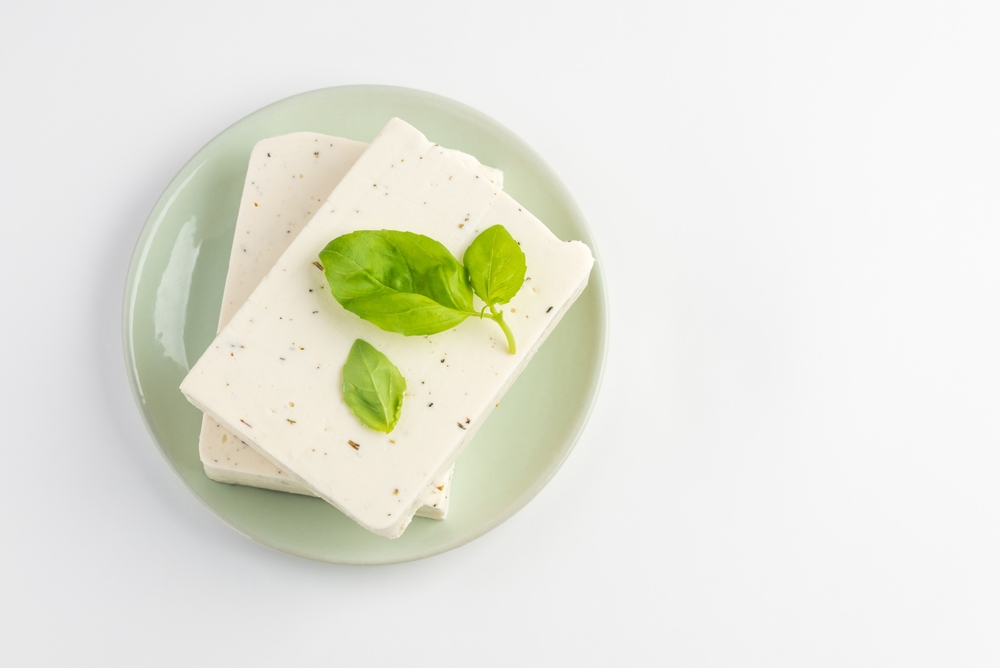 Top view of tofu, paneer or soy cheese with fresh basil leaves in a green plate isolated with copy space
