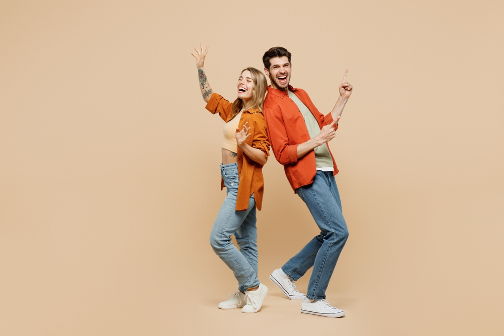 Full body fun young couple two friends family man woman wear casual clothes point index finger aside on area waving hand together isolated on pastel plain light beige color background studio portrait