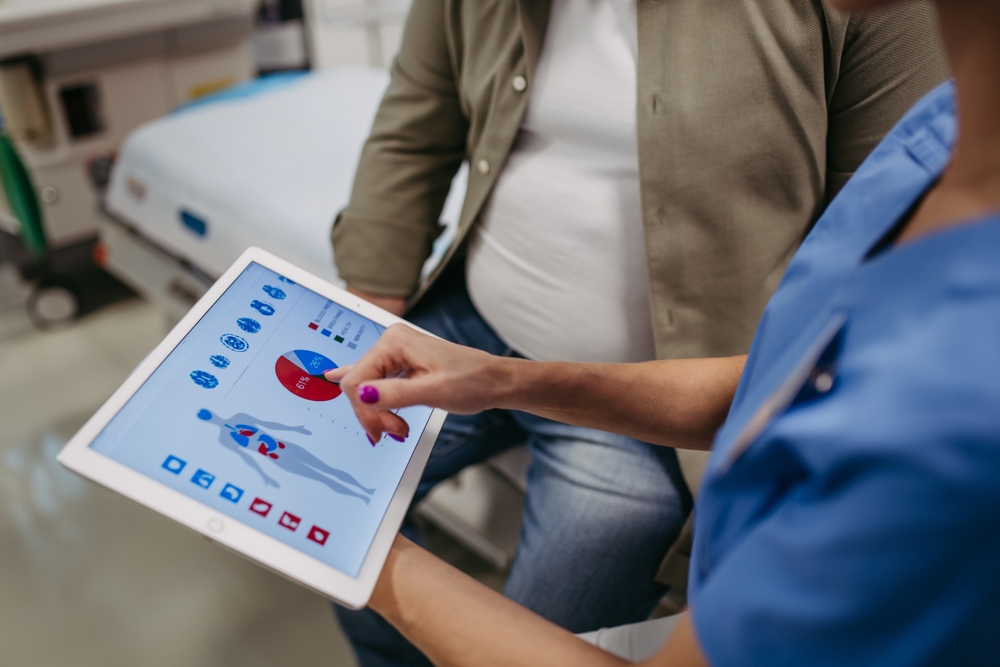 Close up of female doctor consulting with overweight patient, discussing test result in doctor office. Showing medical report on tablet. Obesity affecting middle-aged men's health. Concept of health
