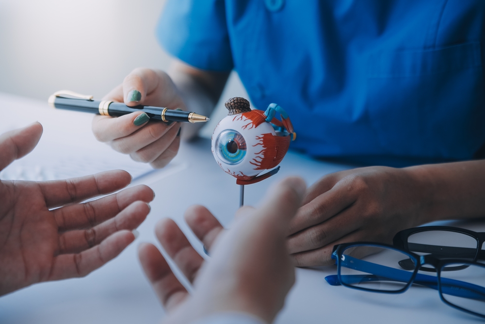 Close-up of Asian female doctor talking with elderly patient showing eyeball model and explaining eye disease in hospital
