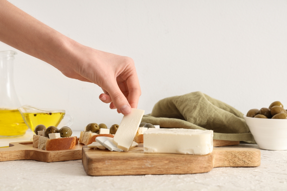 Female hand with wooden board of tasty feta cheese on white background
