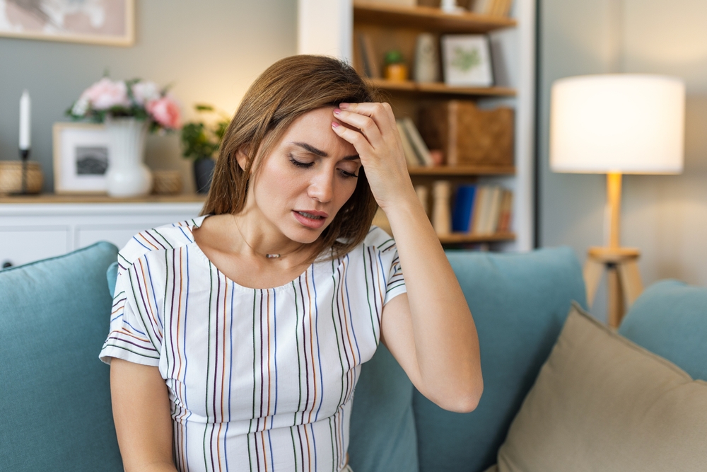 Headache. Close-up photo of a young woman, who is sitting on a sofa , touching her head while suffering from a migraine.
