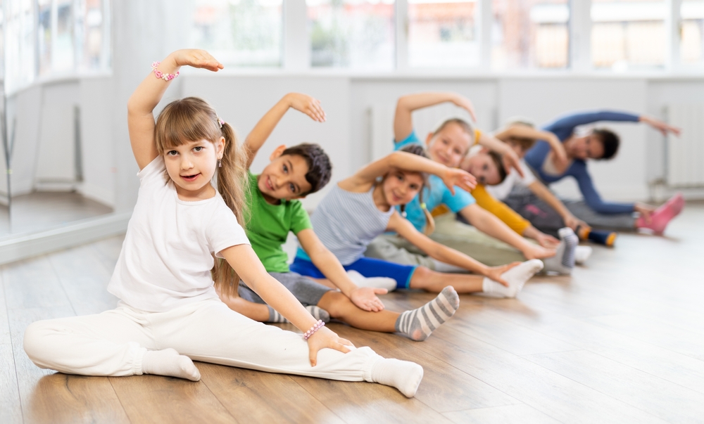 Group of boys and girls with teacher doing warm-up exercises before dancing in studio