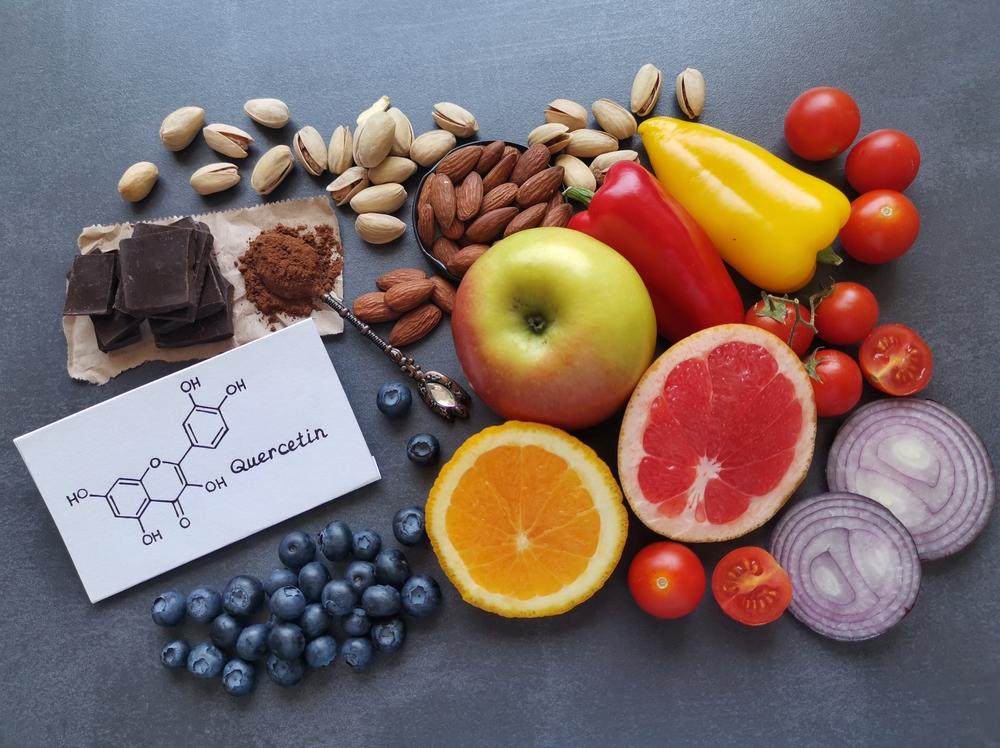 Structural chemical formula of quercetin with fresh fruit and vegetable. Quercetin is a plant pigment (flavonoid). It's found in many plants such as red onion, berries, tomato, nuts, citrus, apple