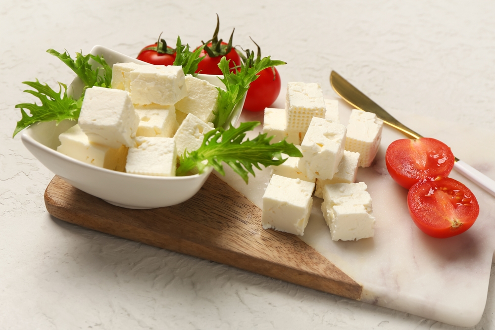 Board with cubes of feta cheese, cherry tomatoes and arugula on white background
