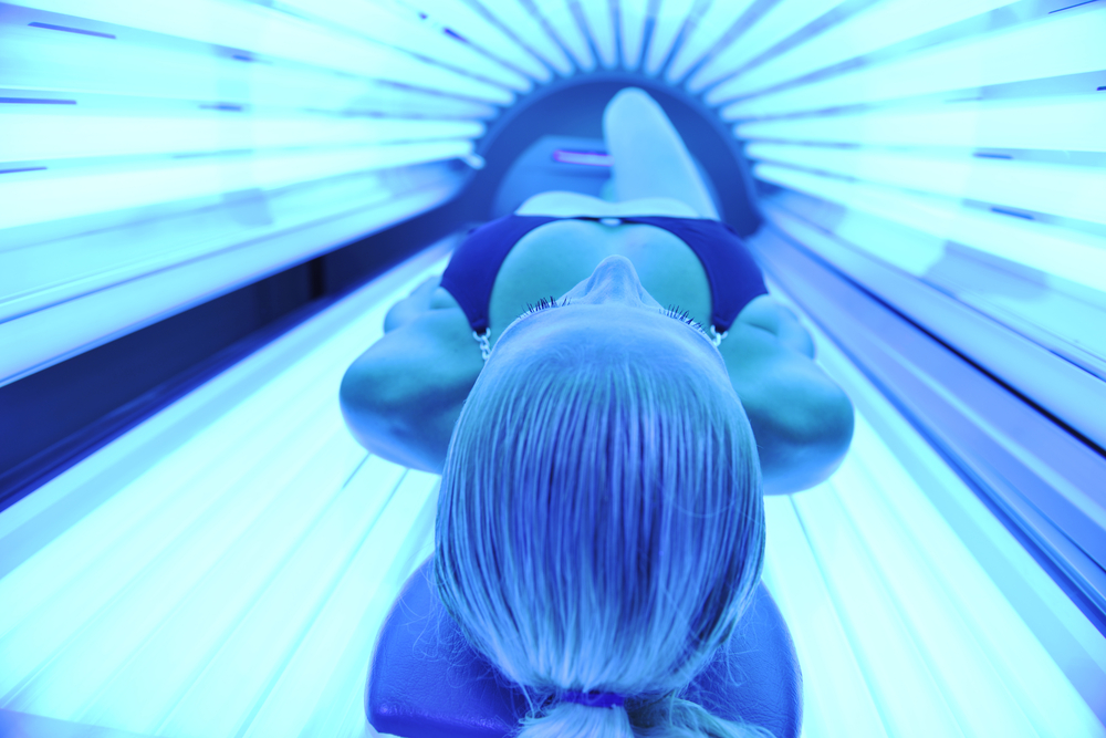 young woman at laying on solarium bed and get brown skin tone ready for summer