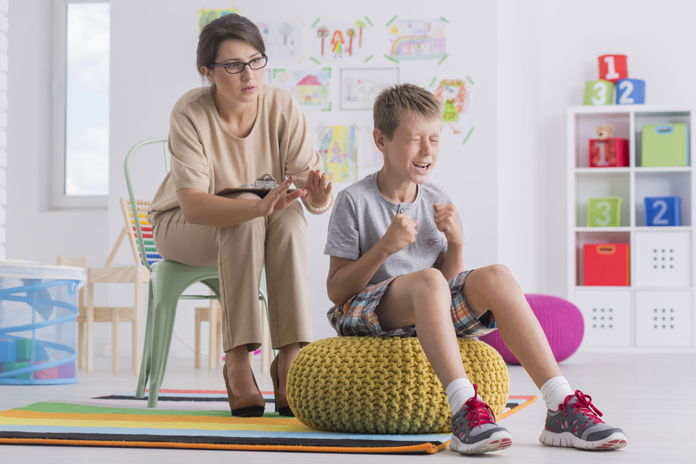 Temper tantrum concept, little angry emotional boy being aggressive during therapy session with child psychotherapist
