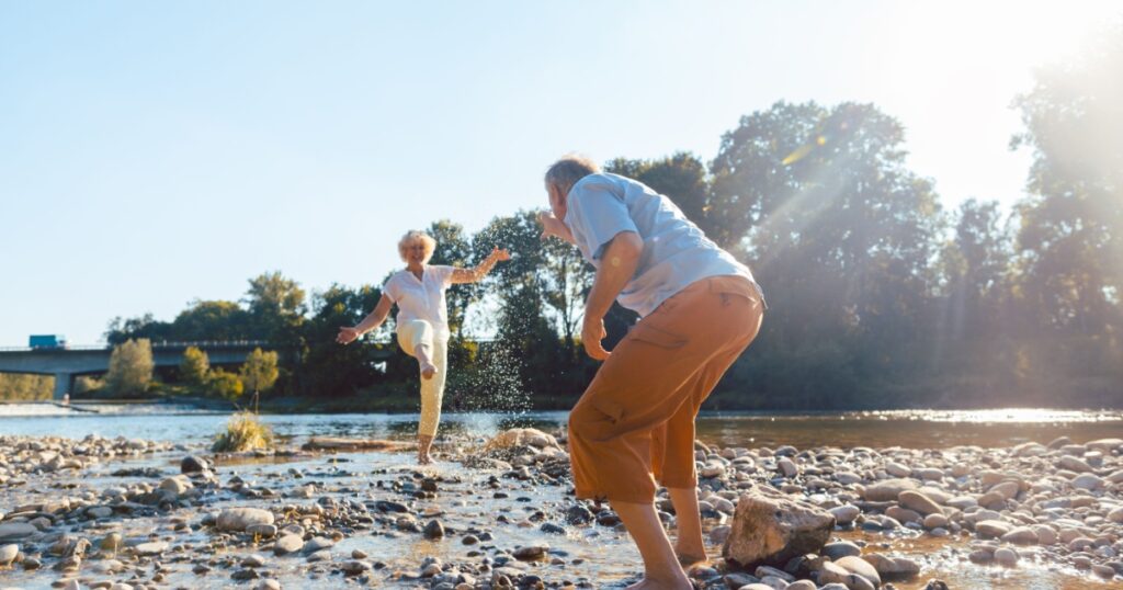 Full length of a funny senior couple playing with water at the river while enjoying their happy relationship in a sunny day of summer