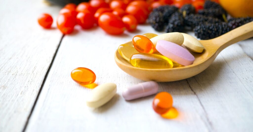 Pills and capsules in wooden spoon with fresh fruits.Multivitamins and supplement from fruits concept.