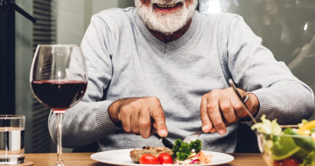 Happy senior man eating pork steak on table at restaurant
