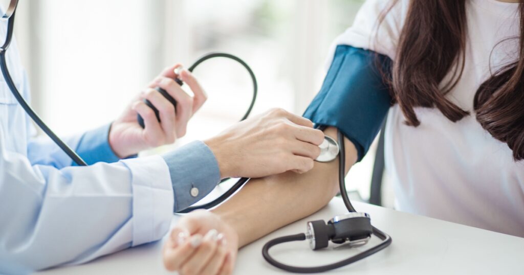 Doctor using sphygmomanometer with stethoscope checking blood pressure to a patient in the hospital.