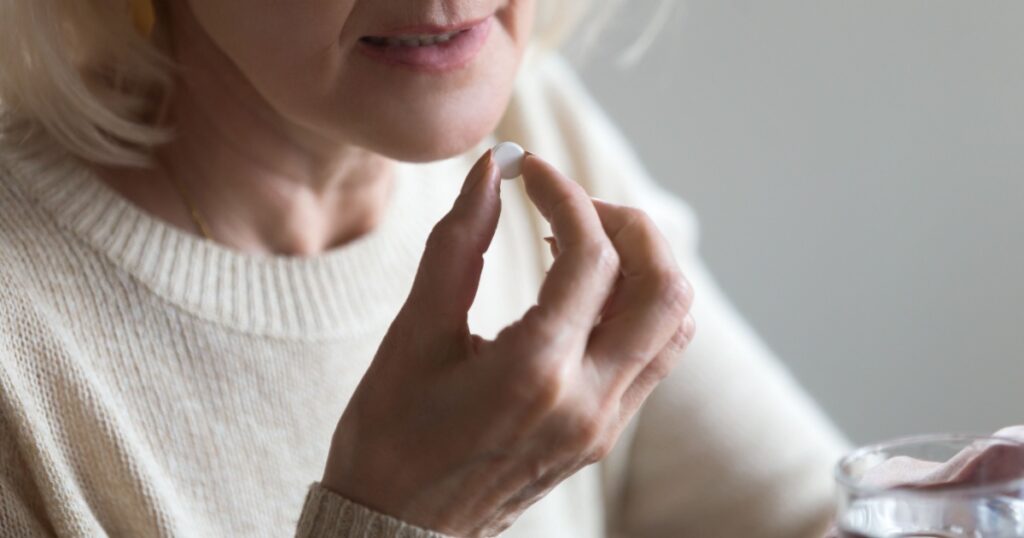 Mature senior middle aged woman holding pill and glass of water taking painkiller to relieve pain, medicine supplements vitamins, antibiotic medication, meds for old person concept, close up view