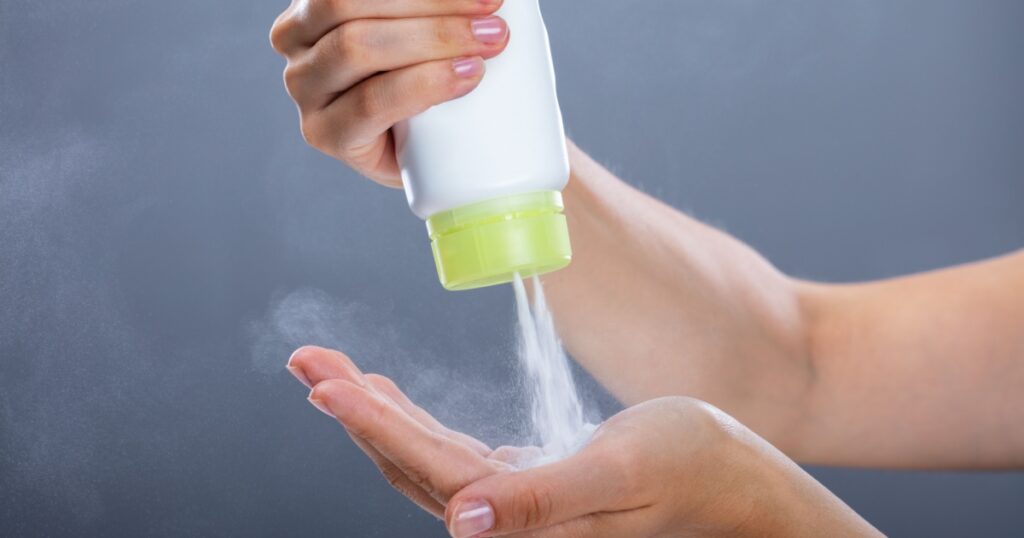 Woman's Hand Using Talcum Powder On Grey Background