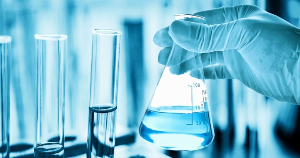 hand of scientist holding flask with lab glassware in chemical laboratory background, science laboratory research and development concept