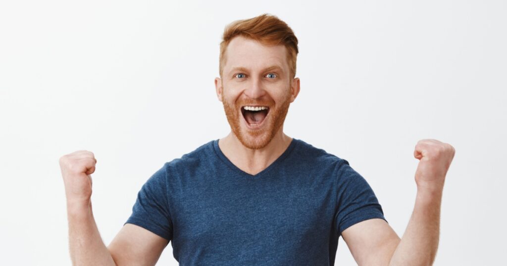 Yeah, good work man. Happy cheerful good-looking redhead strong man, raising clenched fists in hooray gesture, smiling broadly, triumphing from successful deal or great news, being joyful and thrilled