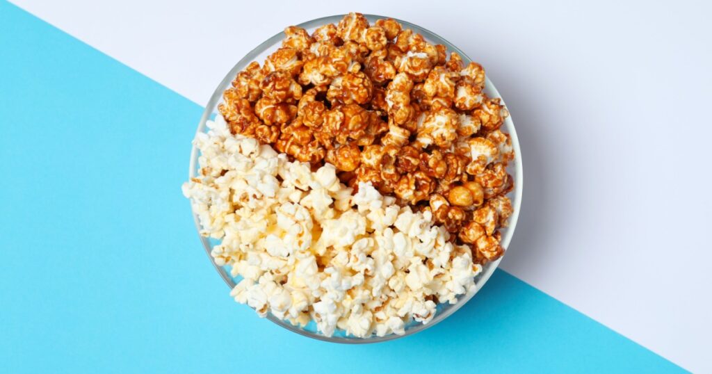 Different kinds of popcorn in bowl on color background, top view