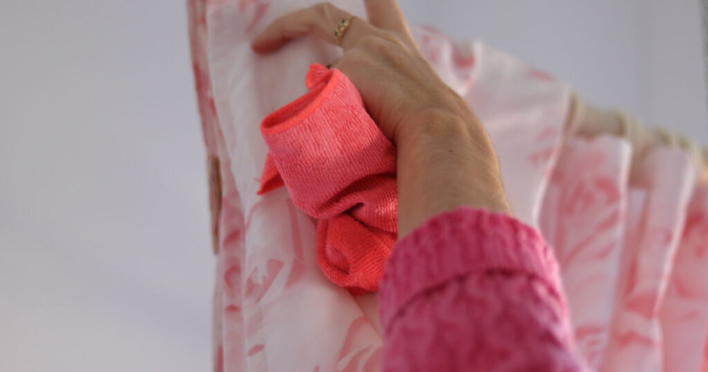 Woman cleaning bathtub curtain using rag cloth and soap spray