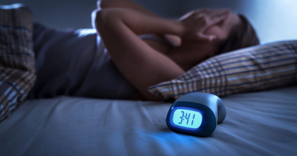 Sleepless woman suffering from insomnia, sleep apnea or stress. Tired and exhausted lady. Headache or migraine. Awake in the middle of the night. Frustrated person with problem. Alarm clock with time.