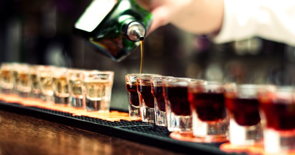 Bartender pours alcoholic drink into small glasses on bar