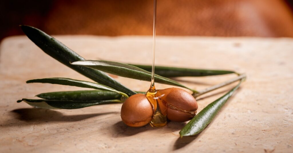 Argan oil, used for cosmetics, pouring over two argan seeds on a stone table.