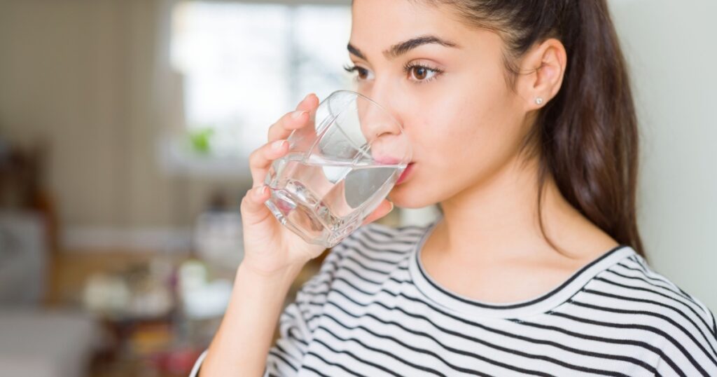 Beautiful young woman drinking a fresh glass of water at home