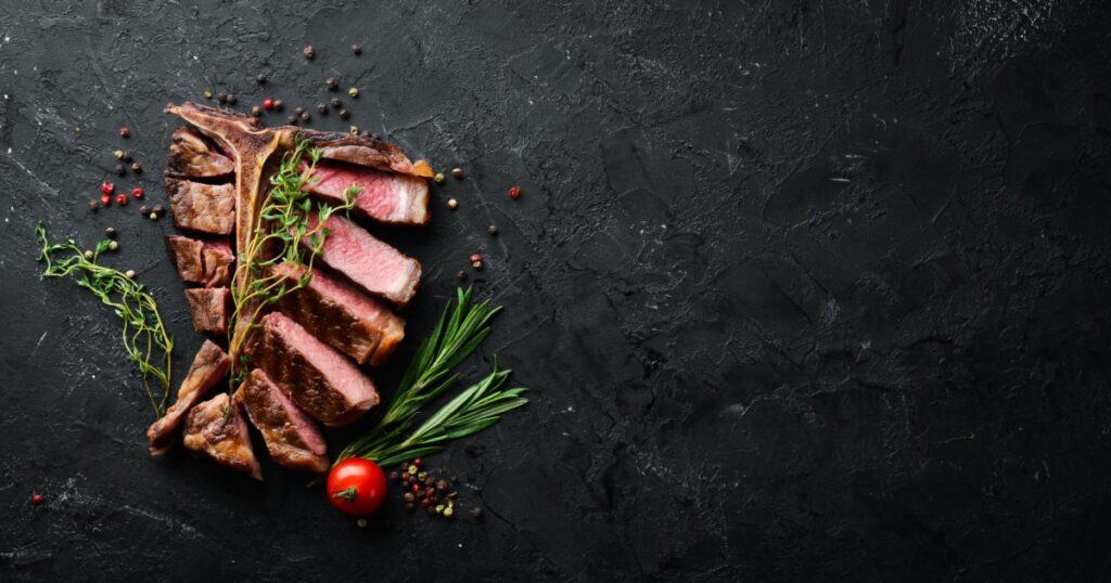 Beef T-Bone steak on a black table. Top view. Free space for text.