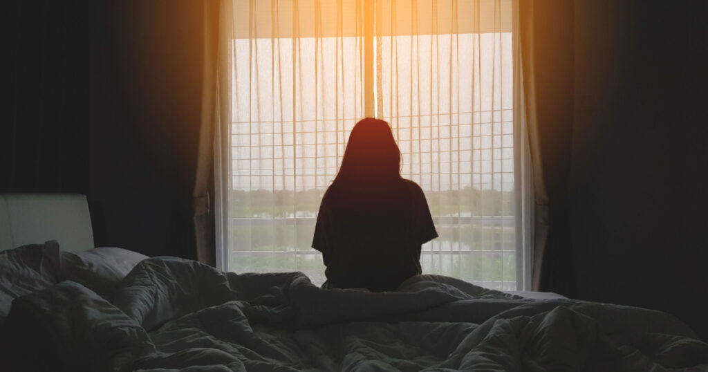 silhouette of woman sitting on the bed beside the windows with sunlight in the morning