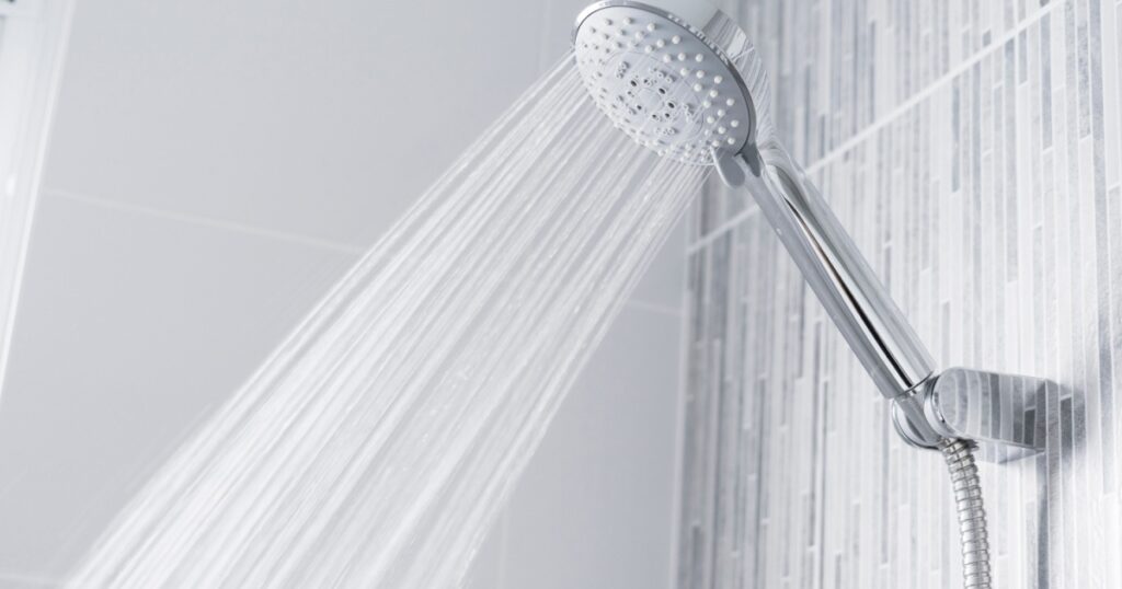 Fresh shower behind wet glass window with water drops splashing. Water running from shower head and faucet in modern bathroom.