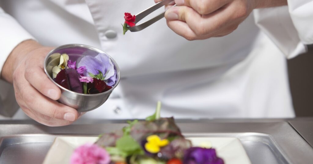 Midsection closeup of male chef arranging edible flowers on salad in commercial kitchen