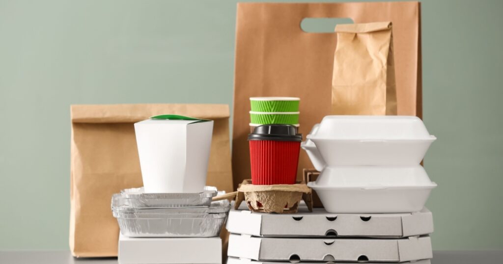Different packages on table against color background. Food delivery service