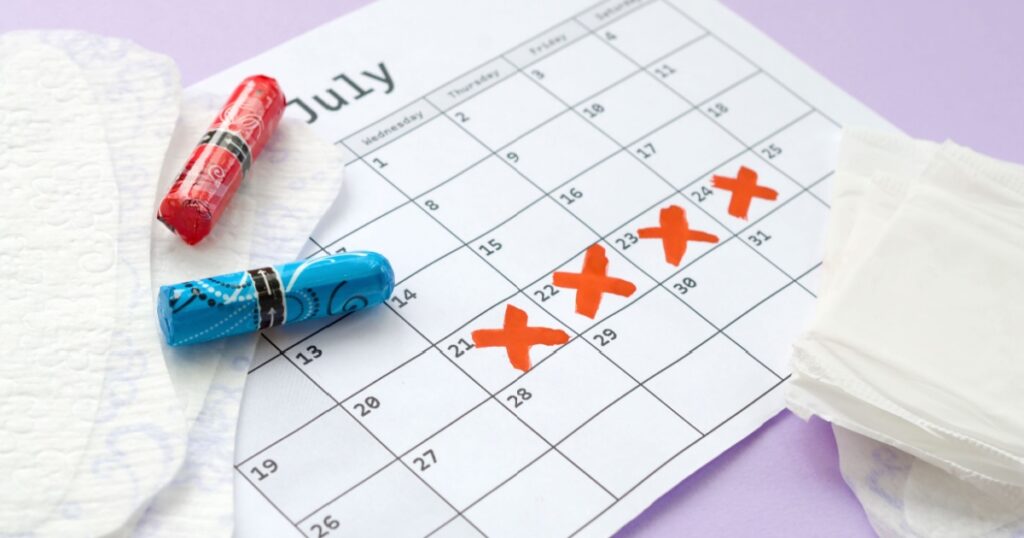 Menstrual pads and tampons on menstruation period calendar with red cross marks lies on lilac background