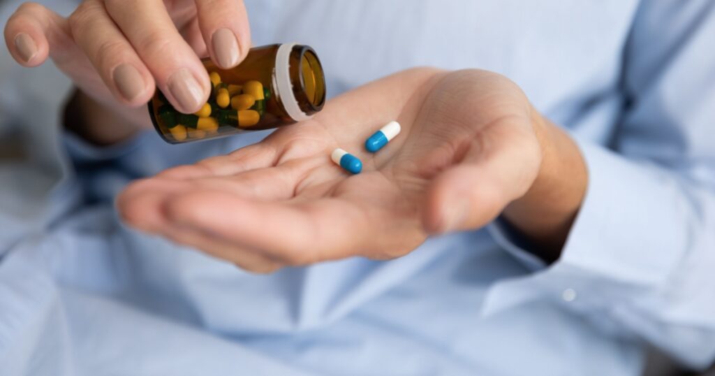 Elderly sick ill woman hold two pills on hand pouring capsules from medication bottle take painkiller supplement medicine, old senior people pharmaceutical healthcare treatment concept, close up view