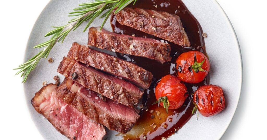Grilled sliced Beef Steak with tomatoes and rosemary on a plate Isolated on white background top view
