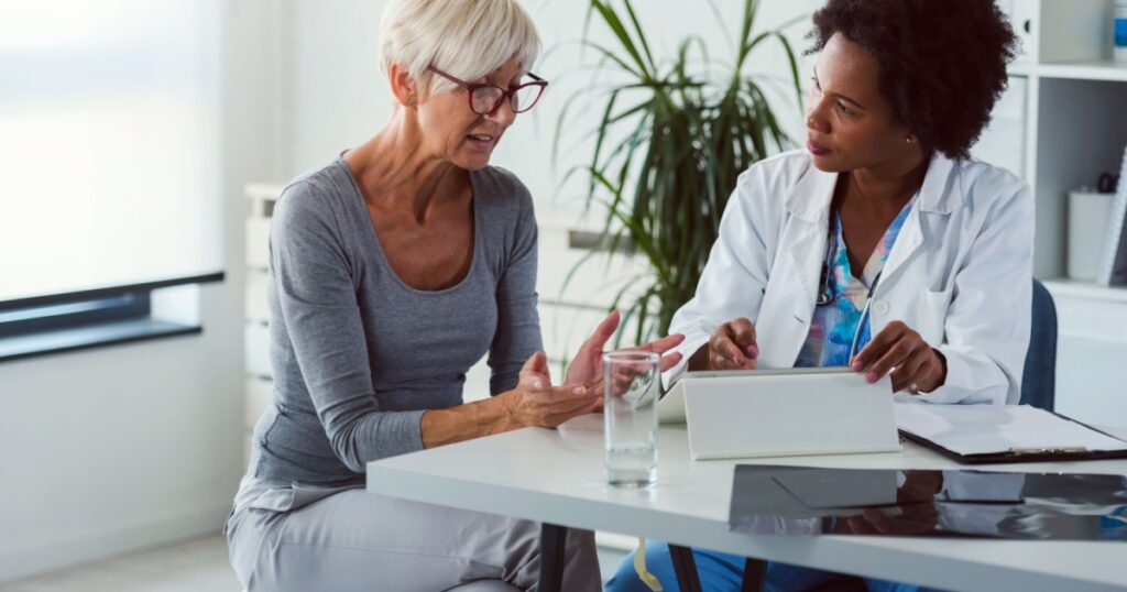 A female doctor sits at her desk and chats to an elderly female patient while looking at her test results