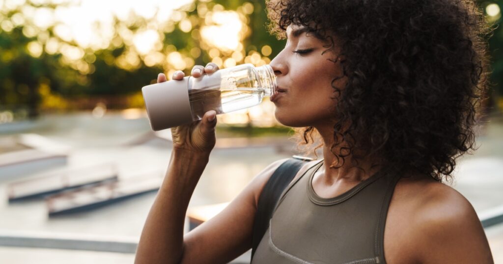 Image of african american sportswoman drinking water while working out on sports ground
