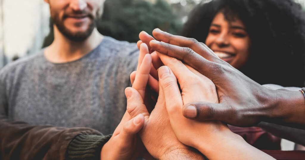 Young happy people stacking hands outdoor - Multiracial students celebrating together - Focus on hands