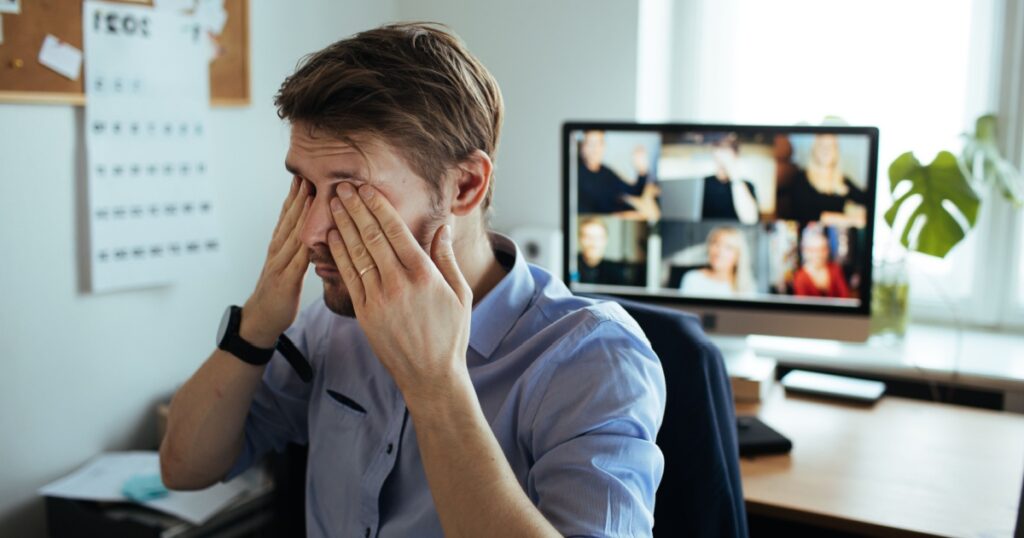 Information overload. Fatigue from work at home. Tired businessman headache while having a video call via a computer in the home office. Remote team meeting video online conference exhausting calls