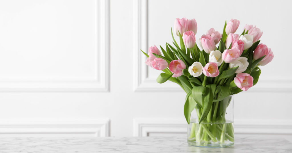 Beautiful bouquet of tulips in glass vase on white marble table. Space for text