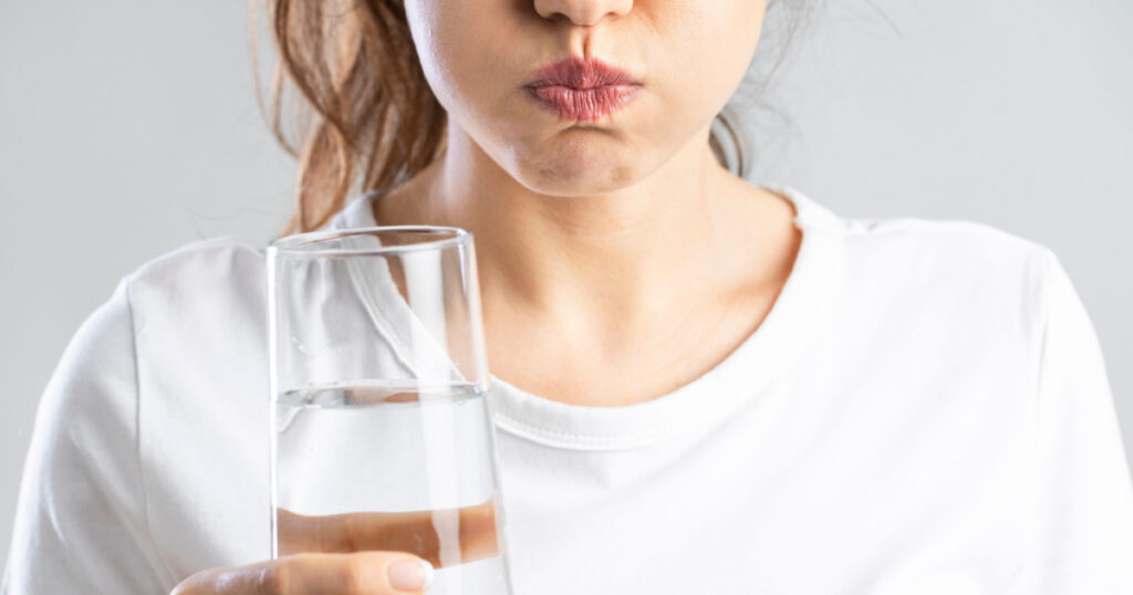 Young woman gargling while using mouthwash from a glass