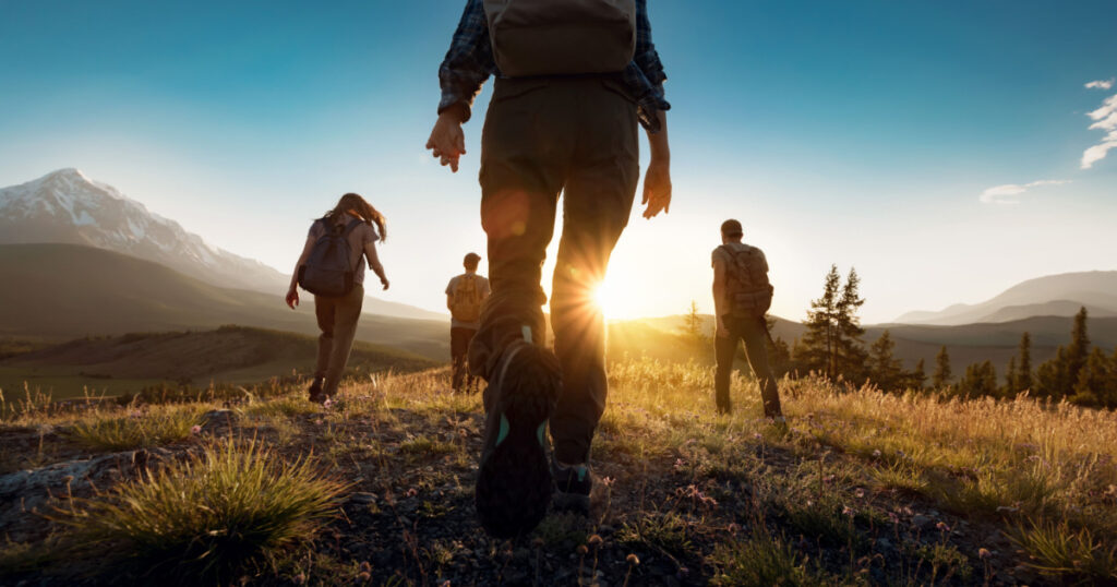 Group of sporty people walks in mountains at sunset with backpacks. Altai mountains, Siberia, Russia.