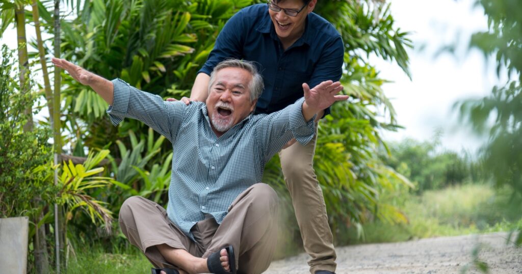 Senior grandfather have fun with riding skateboard togetter young man son in outdoor garden - family activity outdoor concept