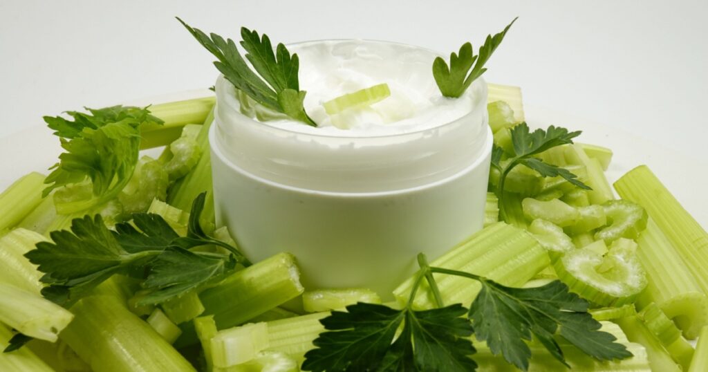 Jar of a natural celery-infused cream, and fresh celery stalks, background